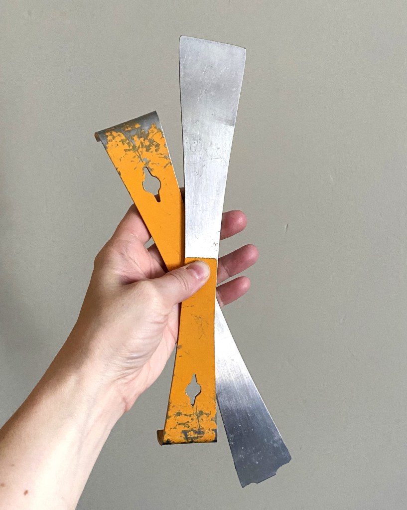 Two flat pry bars called hive tools with yellow handles crisscrossed.